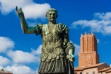 Trajan emperor of Ancient Rome old statue with medieval Tower of Militia in the background along Imperial Fora Road in the historic center of Rome