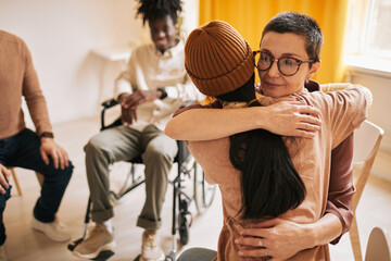 Portrait of female psychologist embracing young woman during therapy session in support group, copy space