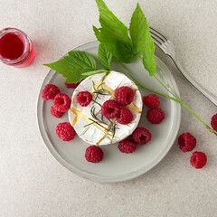 dessert plate with baked camembert with raspberries and rosemary on a light table