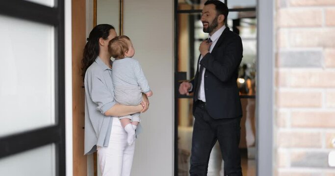 Businessman going out at work, kissing and saying goodbye to his wife and baby at the hallway of the house. Farewell with a family and daily morning routine