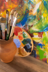 Paint brush in clay jug and palette on wooden table background. Oil painting and art still life