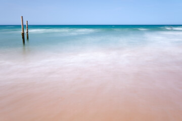 Fotografía de larga exposición de una playa con un par de postes en medio del agua turquesa