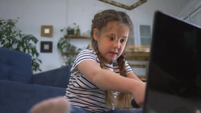 Happy girl playing video games with a joystick. Child gambling addiction. Happy little girl playing video game home. Concept of child gambling addiction. Happy little girl learning to work on laptop