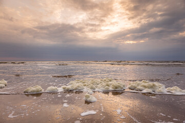 Dramatic sunset overcast sky with sunlight coming through reflecting in the washed up sea foam on...
