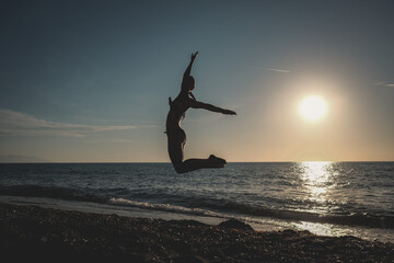 dancer jumps on the beach at sunset over the sea, ballerina salta sulla spiaggia al tramonto sul mare