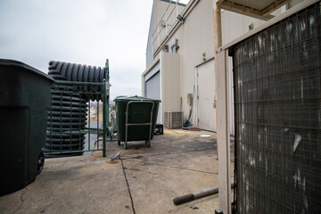 Cart, air conditioner unit, trash bin, with doors behind shopping center building on cloudy day in winter