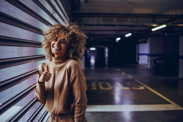 Smiling mixed race rap girl leaning on garage door and showing thumbs up.