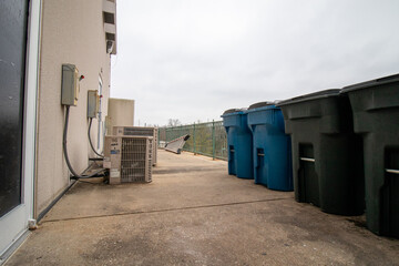 Trash cans and air conditioner unit behind shopping center building on cloudy day in winter