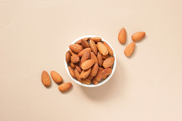 top view of roasted almonds in circle white ceramic bowl placed on brown background.