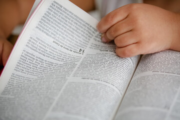 Criança em cima da mesa lendo a bíblia sagrada e folheando.