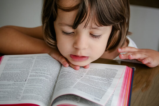 Criança em cima da mesa lendo a bíblia sagrada e folheando.