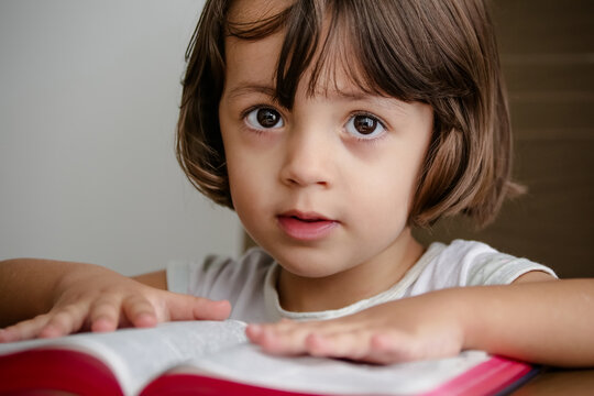 Criança em cima da mesa lendo a bíblia sagrada e folheando.