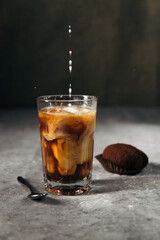 Composition of cold coffee in a tall glass with milk and chocolate cookies on a gray dark background with copy space. 
milk is poured into coffee