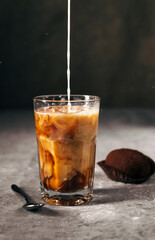 Composition of cold coffee in a tall glass with milk and chocolate cookies on a gray dark background with copy space. 
milk is poured into coffee