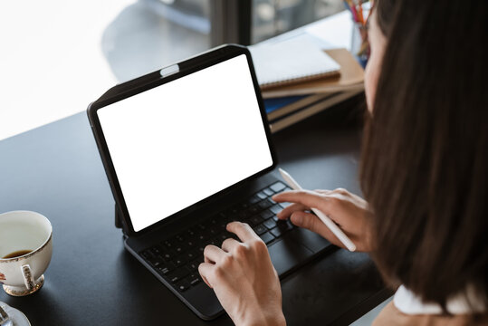Image of a businesswoman sitting in working at the office holding a pen using tablet blank white screen. Mock up.