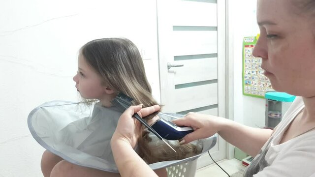 a mother cuts her child's long hair for free with an electric hair clipper, which falls on a special hair stand to avoid soiling clothes and the floor