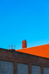 Obraz premium Cityscape: red brick wall, iron staircase to the roof, disassembled chimney and blue sky
