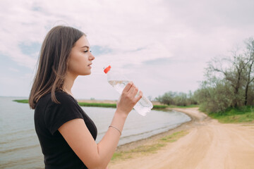 A young girl of Caucasian appearance drinks water on the river bank