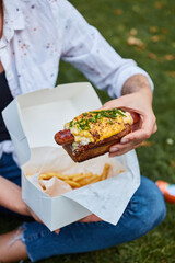 young girl holding delicious hot dog and fries in the garden