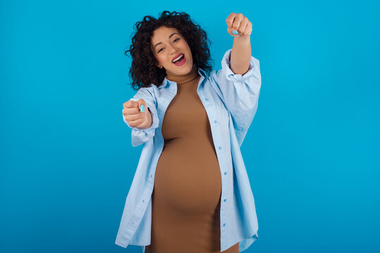 Young Arab Pregnant Woman Wearing Dress Against Blue Wall  Imagine Steering Wheel Helm Rudder Passing Driving Exam Good Mood Fast Speed