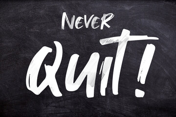 Never Quit typography poster on a black board using white color. Used as an inspirational background or as a motivation quote design for concepts like determination, persistence and success mindset.