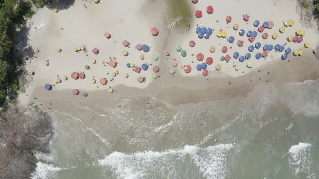 Vue a&eacute;rienne bas en haut des vagues de l'oc&eacute;an, des parasols, des palmiers verts sur la plage.. &Eacute;t&eacute; &agrave; Praia Itacare Bahia, Br&eacute;sil. Paysage tropical avec palmiers, personnes, parasols, sable, eau
