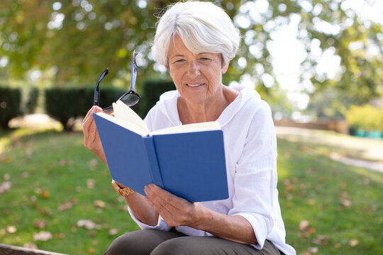 Mature Blonde Woman Reading A Book In The Garden