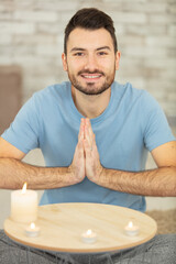 smiling man with hands in prayer position by lit candles