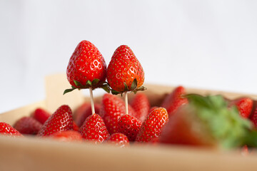red strawberries in a wooden box and two strawberries on a toothpicks on a white background