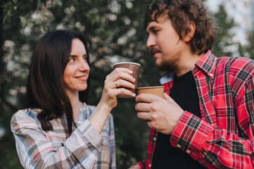 A handsome man and a girl in plaid shirts are resting in nature with hot coffee, tea in an eco-friendly paper cup in their hands. Photography, concept.
