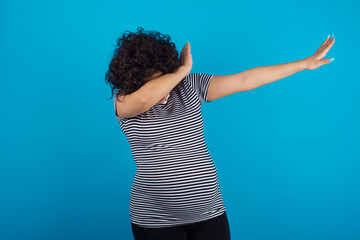Photo of funky young Arab pregnant woman wearing stripped t-shirt standing against blue background...