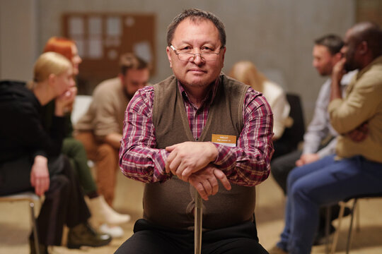 Senior man with crane sitting in front of camera against people describing their problems