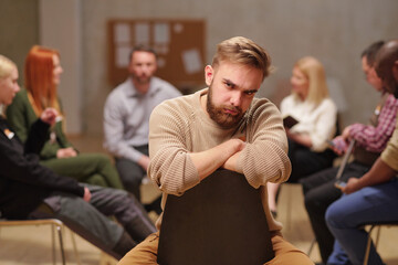 Fototapeta premium Frowning guy with beard sitting on chair during psychological session