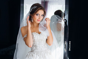 Beautiful young bride in a white wedding dress in the room. Luxurious model reflected in the mirror.