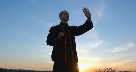 Silhouette of young male kung fu fighter practising alone in the fields during sunset	 - 435496033