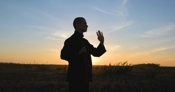 Silhouette of young male kung fu fighter practising alone in the fields during sunset	