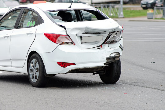 Collision of cars. The white taxi car suffered severe damage to the rear of the body. Broken bumper and trunk lid.