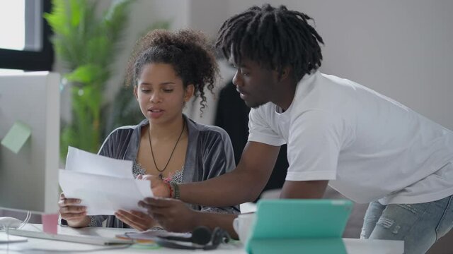 Young couple analyzing business startup plan examining graphs and online data in home office. Concentrated African American man and woman talking discussing idea in the morning indoors