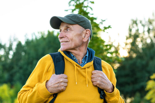 Aged happy traveler in cap and yellow hoodie looking aside in mountains.
