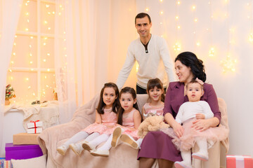 family portrait of a parents and children, sitting on a couch in home interior decorated with lights and gifts