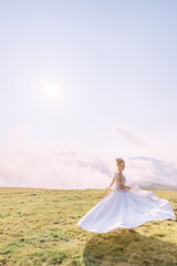 Fototapeta na wymiar beautiful, cheerful bride rejoices, dances, waving her dress against the background of clouds, high in the mountains