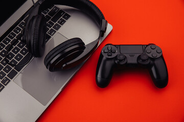 Laptop with headphones, gamepad on red background. Gaming, entertainment or leisure concept