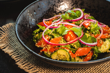 Quinoa salad with tomatoes, avocado, paprika and parsley on black stone plate. Top view.