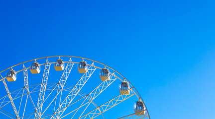 Panoramic ferris wheel carousel with cabins spinning against a blue sky, copy space. Summer fun in the amusement park