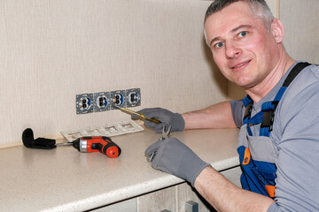 An electrician installs electrical outlets in the kitchen. Tools in hand. Modern design.