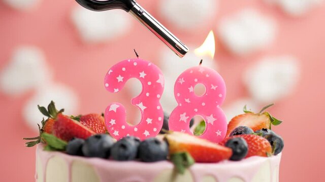 Birthday cake candle number 38. Candle and cake on pink background and fire by lighter. Close-up and slow motion
