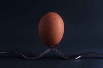 Egg on two forks. Chicken egg stands on two forks. Abstract still life, two forks and egg on a black background. 