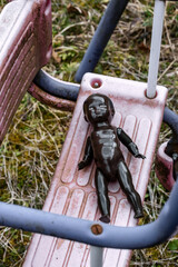 black doll lying on dirty swing at abandoned playground