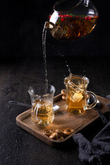 Pour black tea from a transparent teapot into a cup on black backround