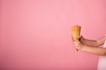 close-up of hands holding a waffle cone on a pink background with space for text